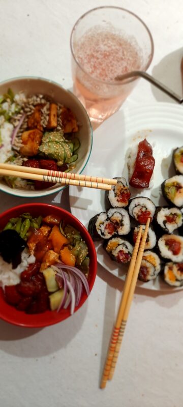 Mesa montada com dois pokes, um prato de sushis veganos utilizando melancia e um copo de soda italiana.